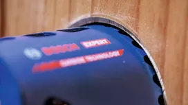 Lame de scie cloche perçant un trou circulaire dans une planche de bois.